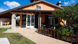 Ein Haus mit überdachter Terrasse, Steinsäulen und einem umzäunten Garten.