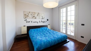 Ein Schlafzimmer mit einem Bett, einer Wandleuchte, einem Fenster und einem Wandbild mit Text.