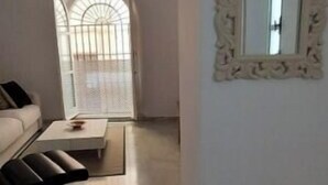 Una sala de estar con un sofá blanco, una mesita redonda y un espejo decorativo en la pared.