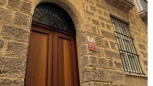 Un edificio de piedra con puerta de madera, una ventana con rejas y un balcón con barandilla de metal.