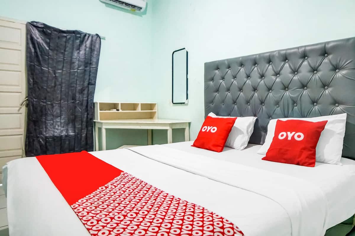 Hotellihuone, jossa on sänky, kaksi punaista koristetyynyä, joissa on «OYO»-merkki, harmaa, kuviollinen pääty, valkoinen yöpöytä ja mustakehyksinen peili.