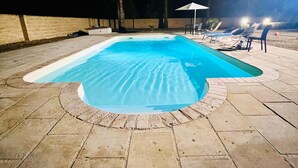 Une piscine dotée d’une plage en pierre, entourée de chaises longues et de parasols.