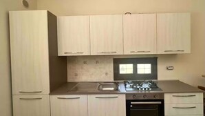 Une cuisine compacte avec des meubles de couleur bois clair, une cuisinière à gaz, un évier et un four encastré.