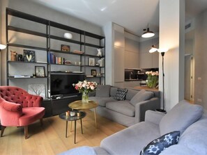 Un salon moderne avec un fauteuil rouge, des canapés gris, une table basse et une bibliothèque.
