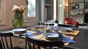 A dining area with a table set for four, a vase of flowers, and a bookshelf in the background.