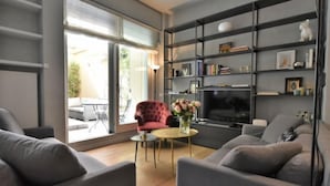 A modern living room with grey sofas, a red armchair, a TV, and a bookshelf.