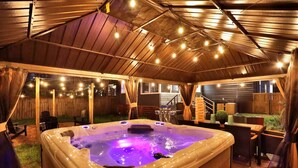 A hot tub with a wooden roof and string lights, surrounded by outdoor furniture and a wooden fence. - Modern Memphis Game House, Hot Tub! Close to Beale (Memphis)