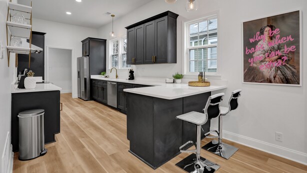 A modern kitchen with dark cabinets, a central island, pendant lighting, and a large window. - Modern Memphis Game House, Hot Tub! Close to Beale (Memphis)