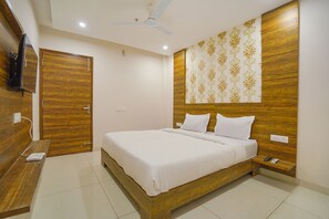 A bedroom with a wooden bed, a nightstand, a ceiling fan, and a TV mounted on the wall. - Fabhotel Hc Mohali Inn (Mohali)