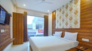 A hotel room with a large bed, wooden headboard, a TV mounted on the wall, and a window with curtains. - Fabhotel Hc Mohali Inn (Mohali)