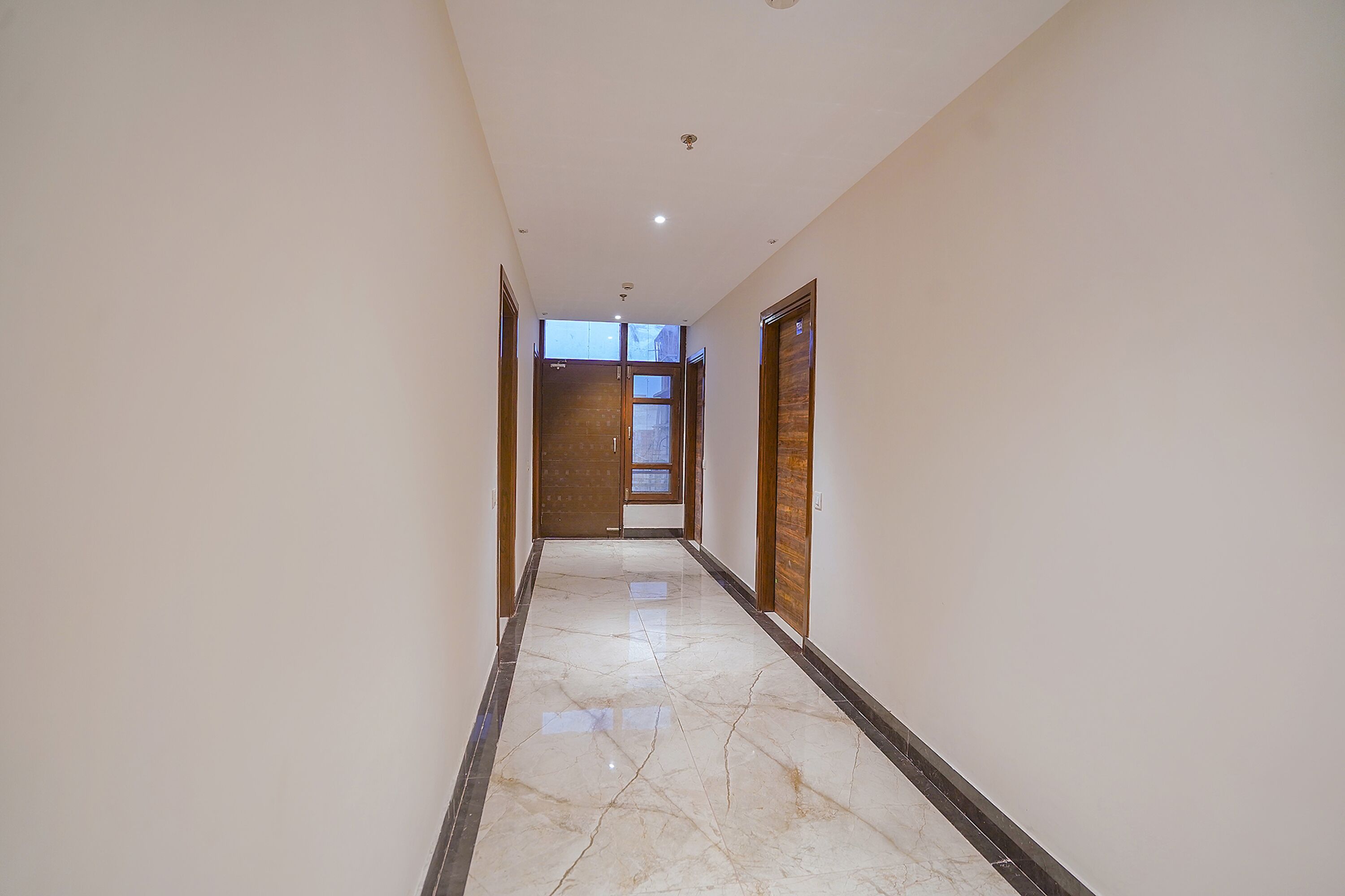 A hallway with a marble floor, wooden doors, and a view of a room at the end.