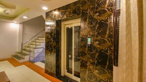 Un intérieur moderne avec un mur en marbre, un escalier et une porte d’ascenseur en verre.