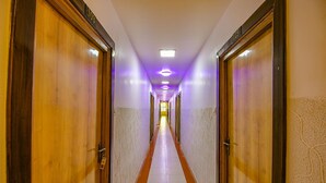 Un long couloir étroit, bordé de portes en bois de chaque côté, qui mène à une pièce lumineuse au bout.
