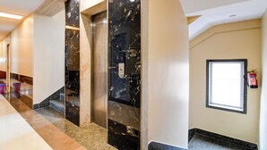 Un pasillo moderno de hotel con paredes de mármol, un extintor y una ventana.