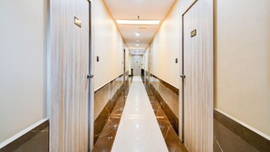 Un pasillo de hotel con puertas numeradas, suelo de mármol e iluminación empotrada en el techo.