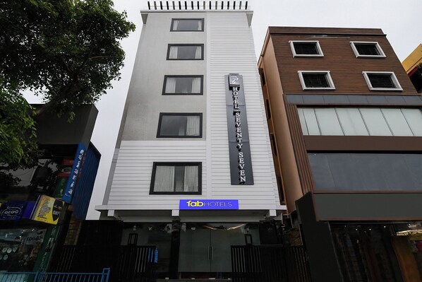 Un hotel de varios pisos con un llamativo letrero que dice 'HOTEL SEVENTY SEVEN', una fachada moderna y una entrada visible con un letrero azul de 'fabHOTELS'.