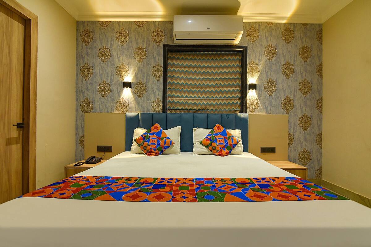 Habitación de hotel con una cama, dos mesitas de noche, aire acondicionado de pared y papel tapiz estampado.