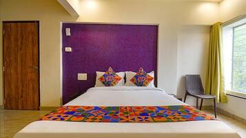 Habitación de hotel con una cama grande, una puerta de madera, un cabecero morado y una ventana con cortinas amarillas.