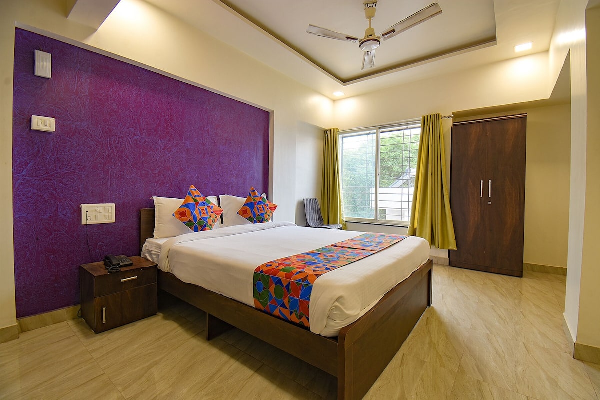 A bedroom with a bed, a nightstand, a wardrobe, a window with curtains, and a ceiling fan.