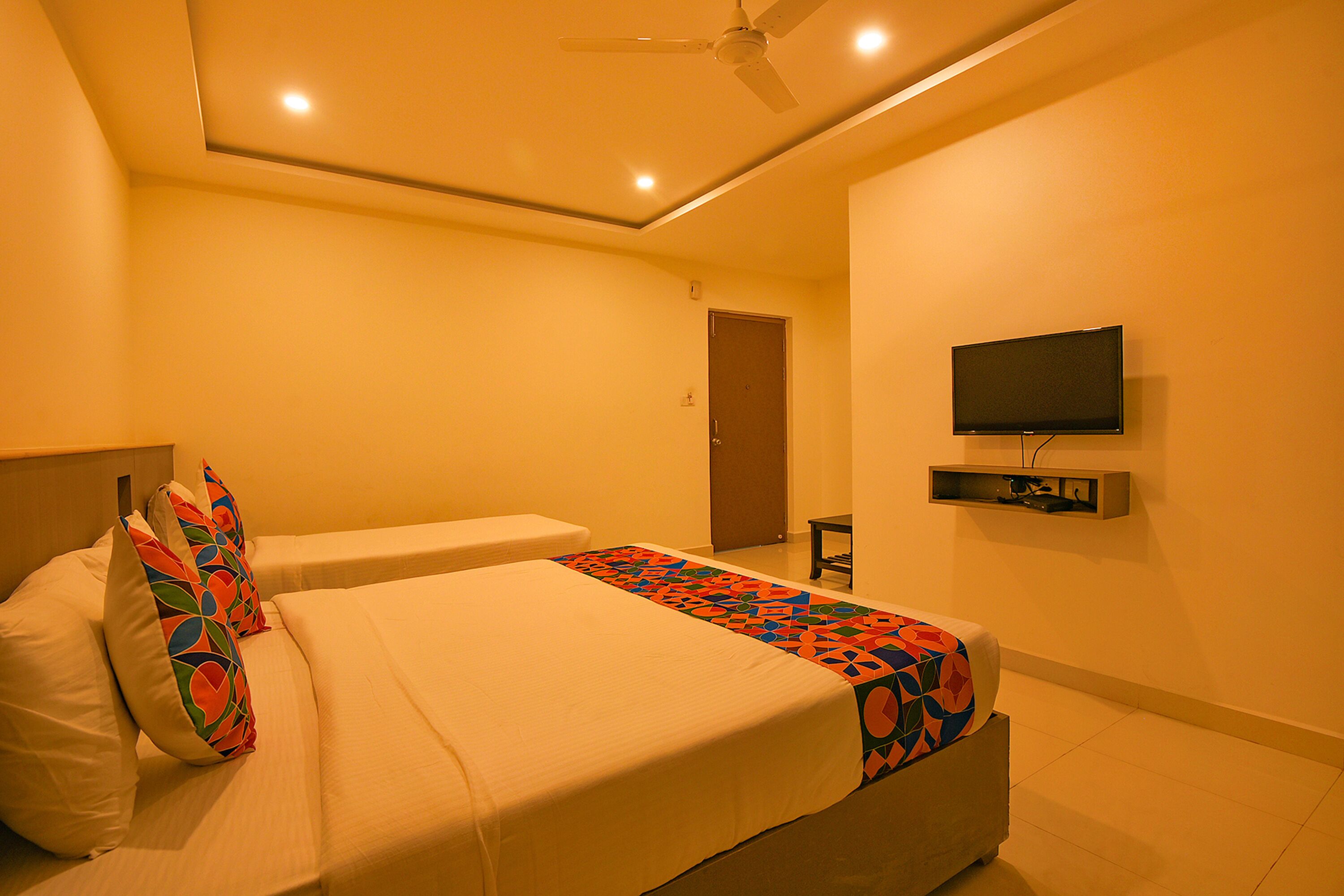 A hotel room with a bed, pillows, a ceiling fan, a TV, and a door.