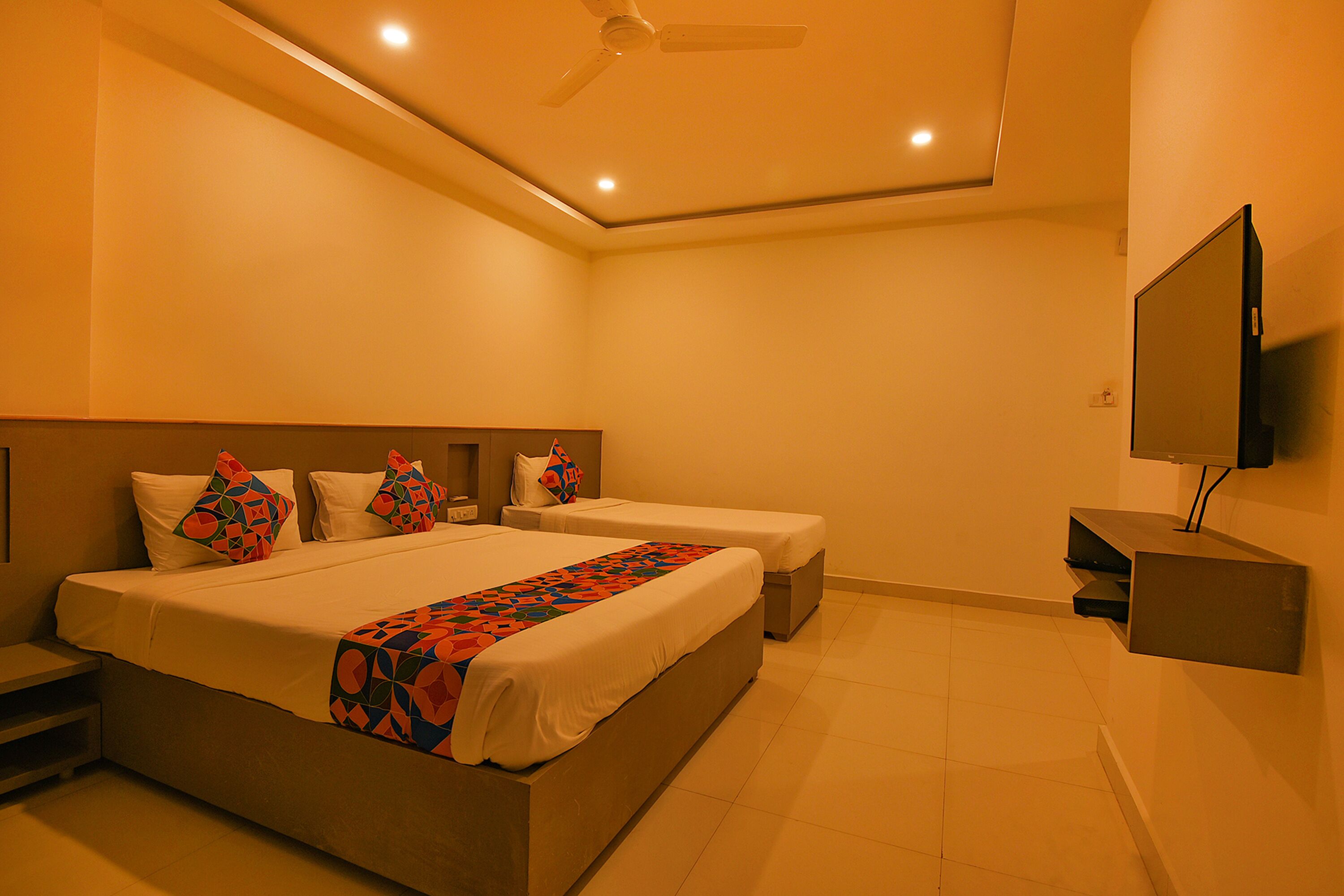 A hotel room with a large bed, two bedside tables, a TV, and a ceiling fan.