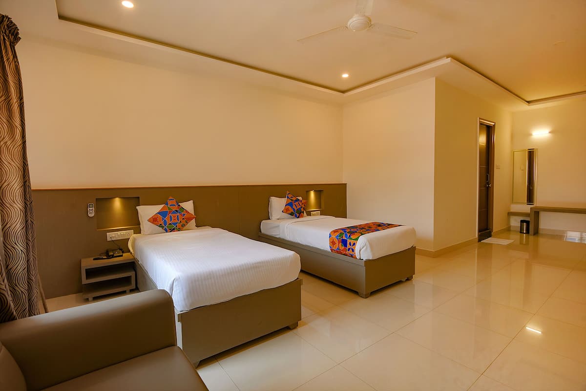 A hotel room with two beds, a small seating area, and a bathroom visible through an open door.