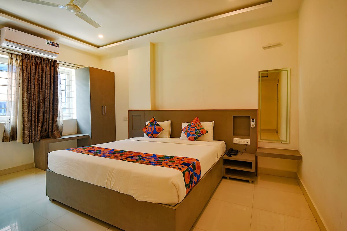 A hotel room with a large bed, a wardrobe, a bedside table with a phone, and a mirror.