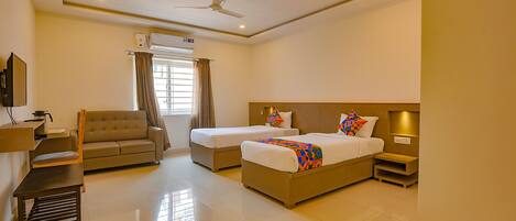 A hotel room with two beds, a sofa, a desk, and a ceiling fan.