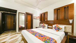 Habitación de hotel con una cama grande, cabecera de madera, ventilador de techo y una colcha estampada.