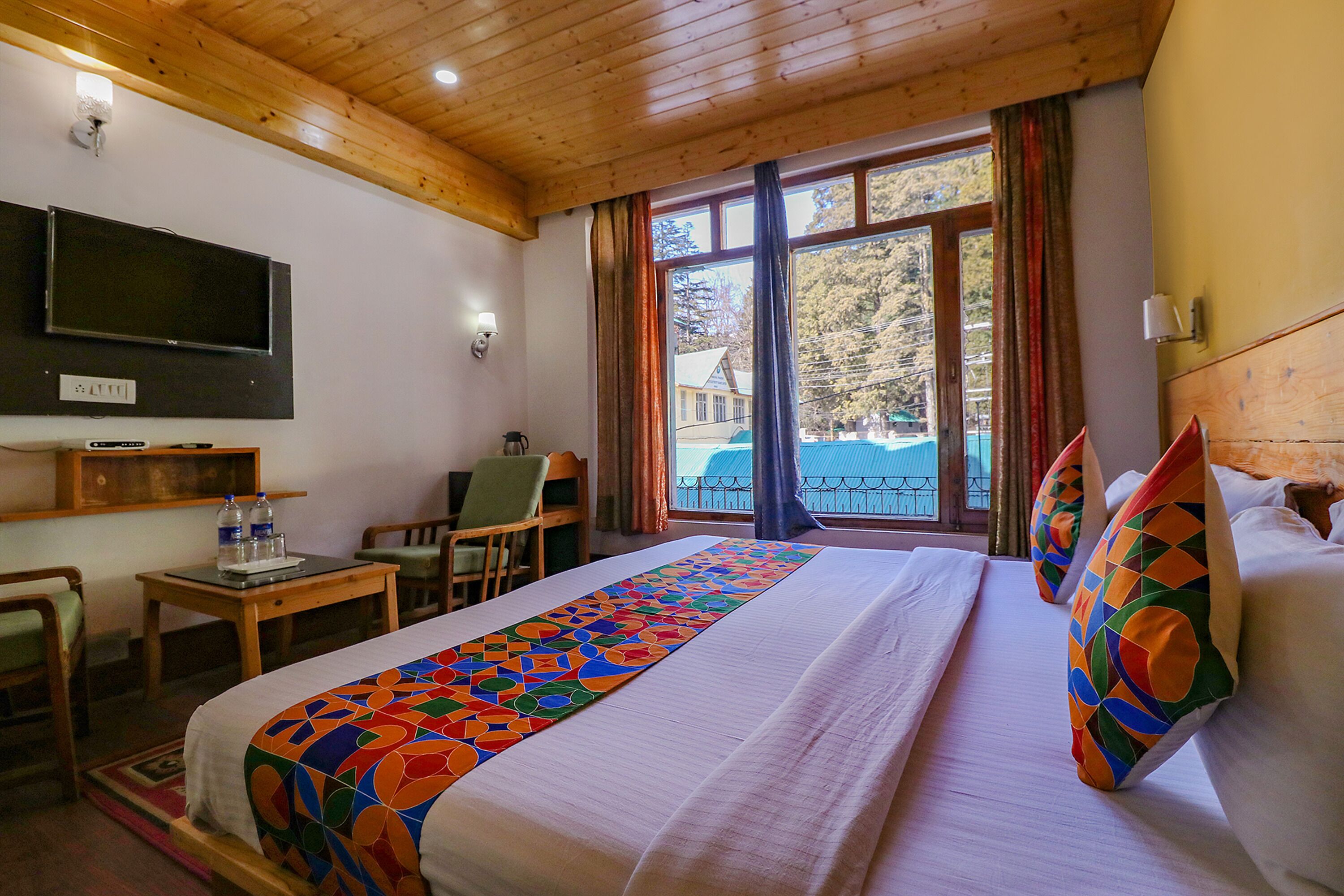 A hotel room with a large bed, a desk, a chair, a TV, and a window with curtains.