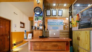 A hotel reception desk with a clock, a sign for Hotel Shandela, a laptop, and a QR code for check-in. - Fabhotel Shandela (Manali)