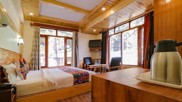 A wooden cabin room with a bed, a desk, a chair, a television, and a coffee pot. - Fabhotel Shandela (Manali)