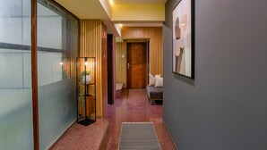 A hallway with a wooden door, a small seating area with cushions, and a framed picture on the wall. - Fabexpress Jayshree (Mumbai)