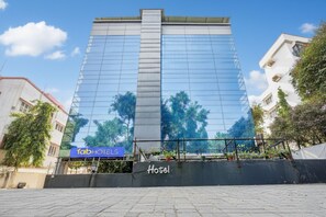 A modern hotel with a reflective glass facade, a sign for 'fabHOTELS' at the base, and a 'Hotel' sign on the ground. - Fabexpress Jayshree (Mumbai)