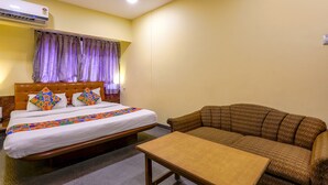 A hotel room with a bed, a sofa, and a small table. - Fabexpress Jayshree (Mumbai)