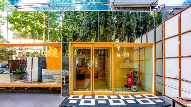 A modern building with a glass entrance, a green mat at the entrance, and a fire extinguisher inside. - Fabexpress Jayshree (Mumbai)