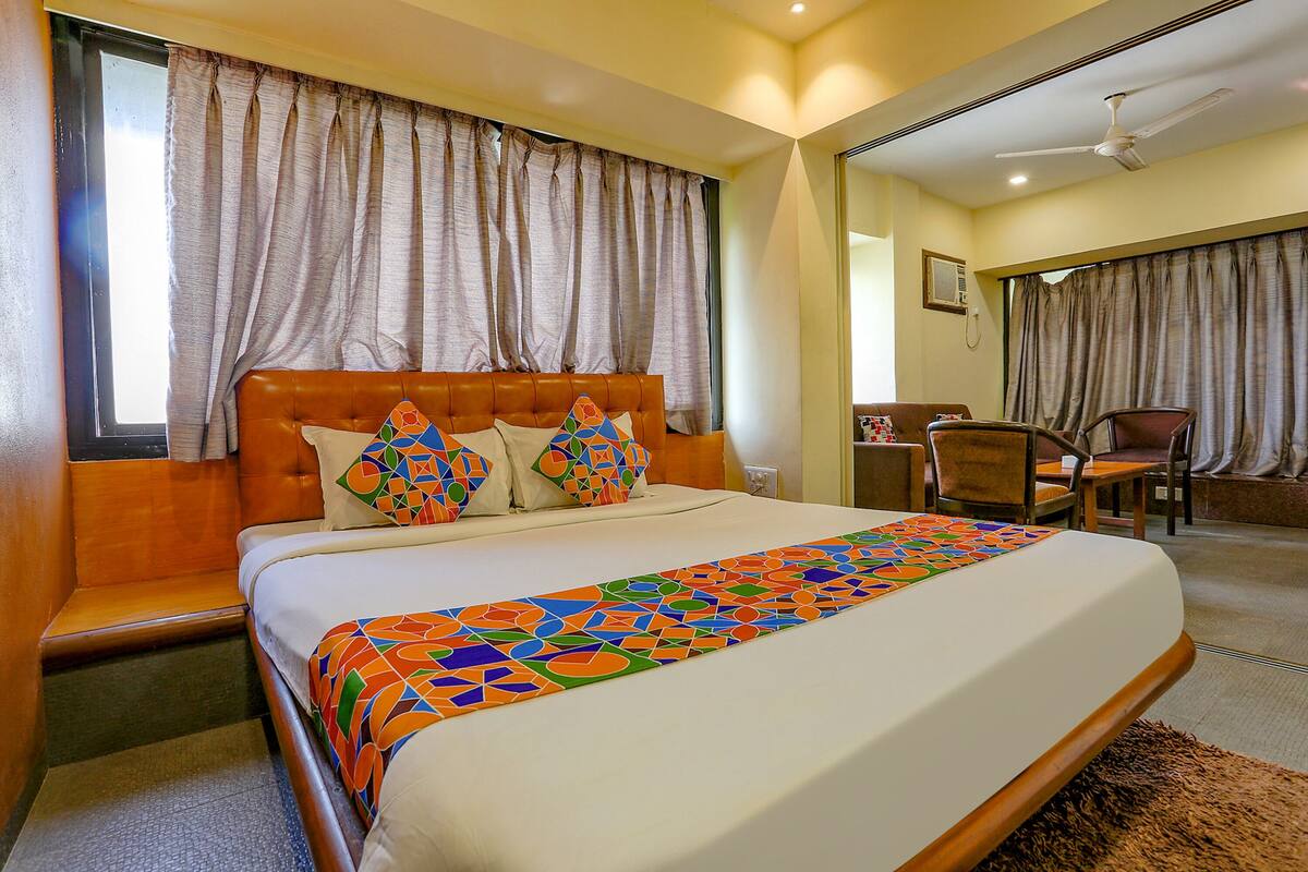 A hotel room with a large bed, a wooden headboard, and a colorful bedspread.