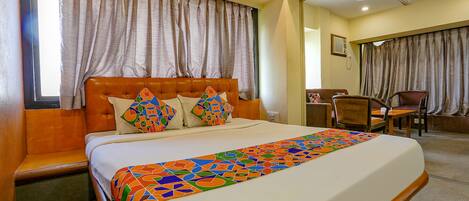A hotel room with a large bed, a wooden headboard, and a colorful bedspread.