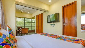 A hotel room with a bed, a TV mounted on the wall, a wooden door, and a window. - Fabexpress Jayshree (Mumbai)