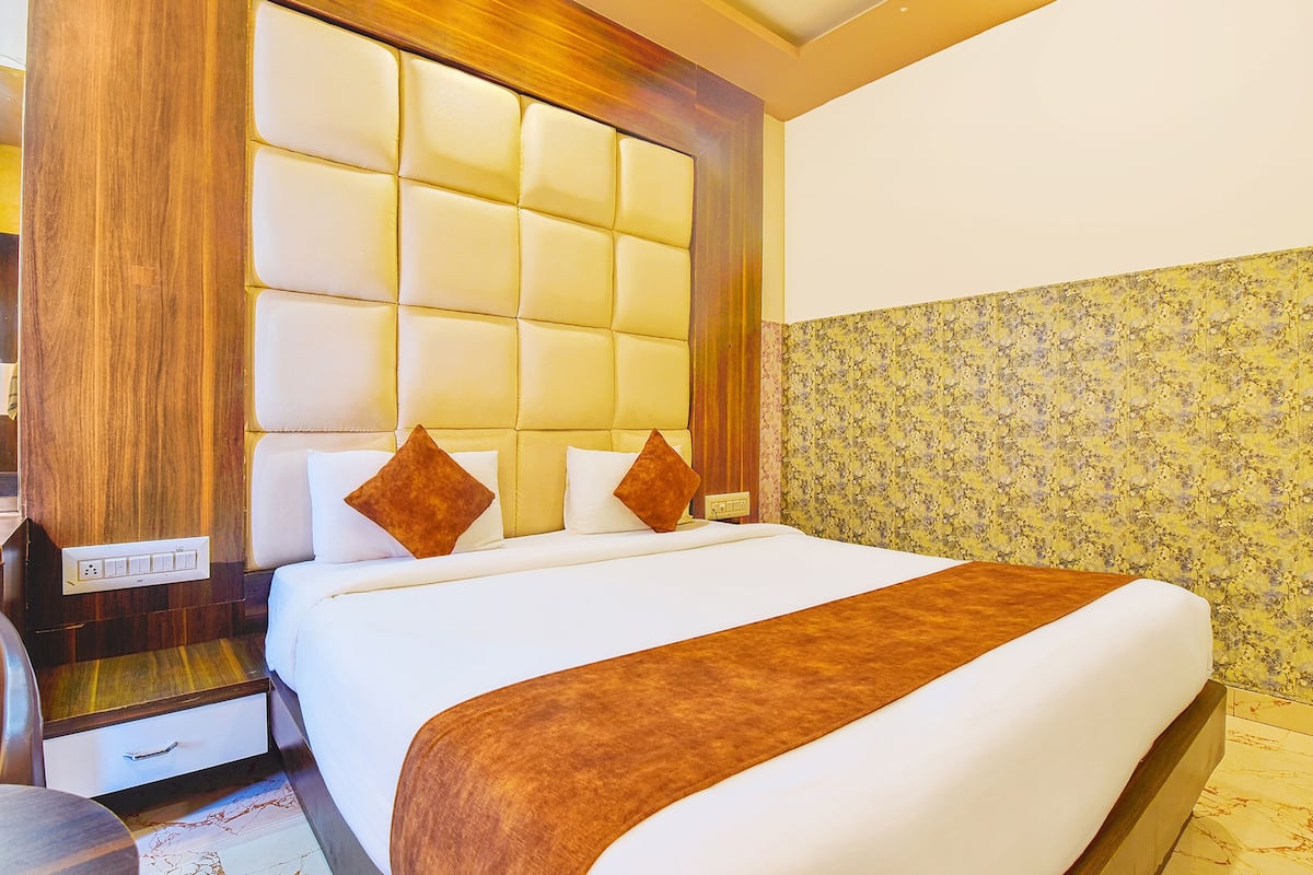 Ein Hotelzimmer mit einem großen Bett, einem hölzernen Kopfteil, einem Nachttisch und einer Wand mit floralem Muster.