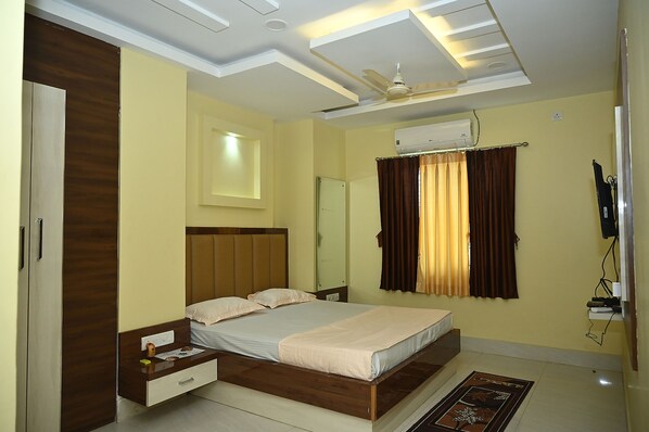 A bedroom with a bed, a nightstand, a wardrobe, an air conditioning unit, and a ceiling fan. - Fabhotel Golden Bliss (Bhubaneshwar)