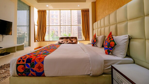 Habitación de hotel con una cama grande, un televisor a la izquierda y una ventana con cortinas.