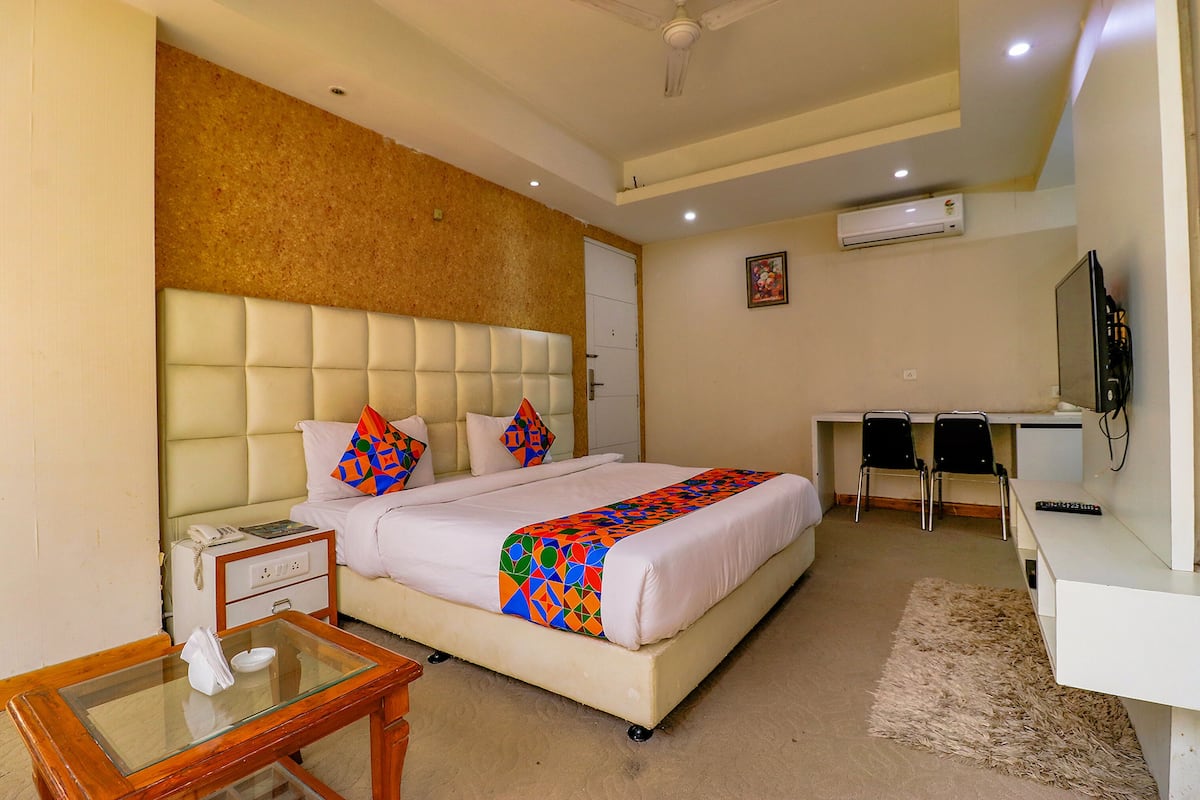 A hotel room with a bed, bedside table, desk, chairs, and a television.