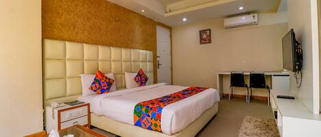 A hotel room with a bed, bedside table, desk, chairs, and a television.