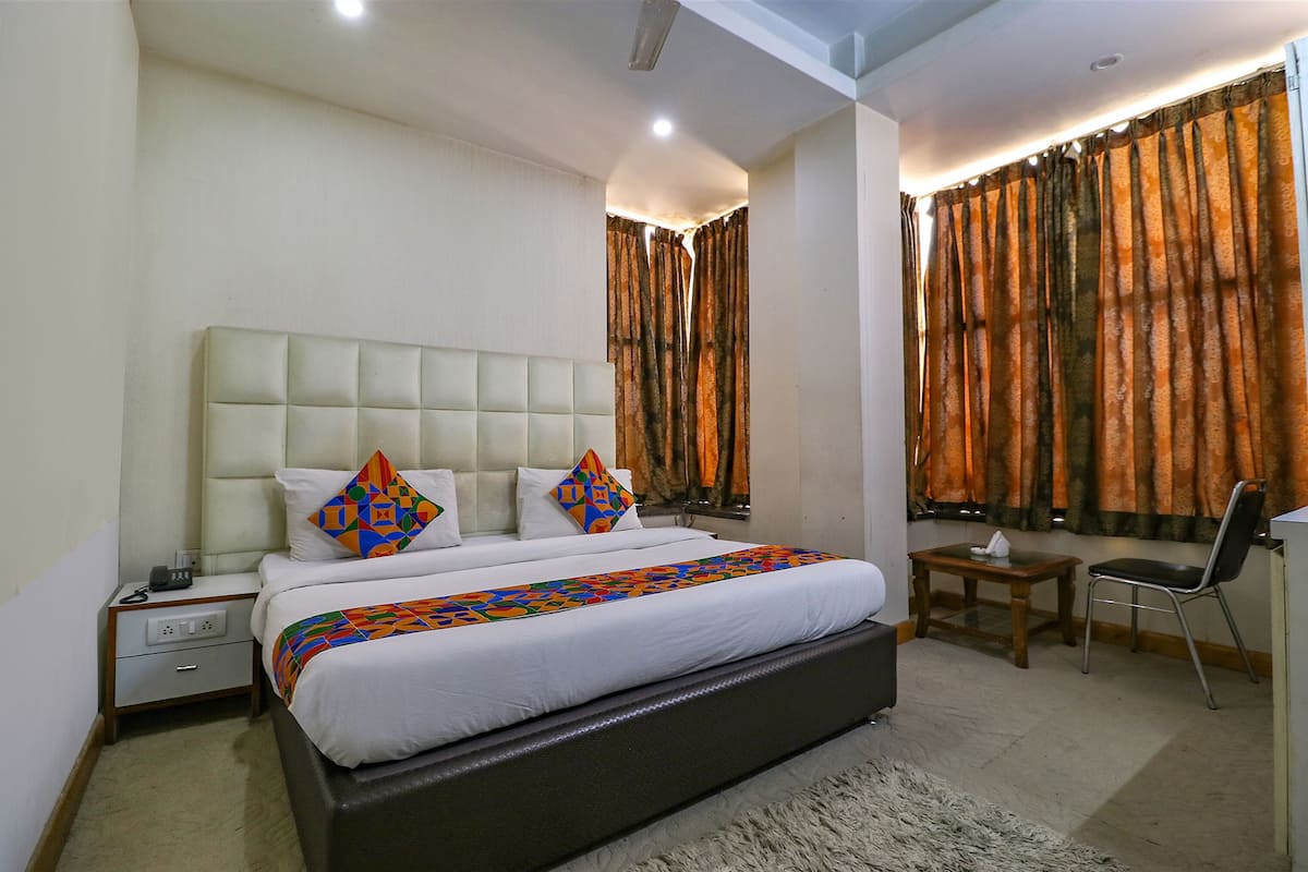 A bedroom with a large bed, a bedside table, a chair, and curtains.