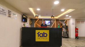 Una recepción de hotel con un letrero de 'fab hotels', un extintor y una pantalla digital sobre el mostrador.
