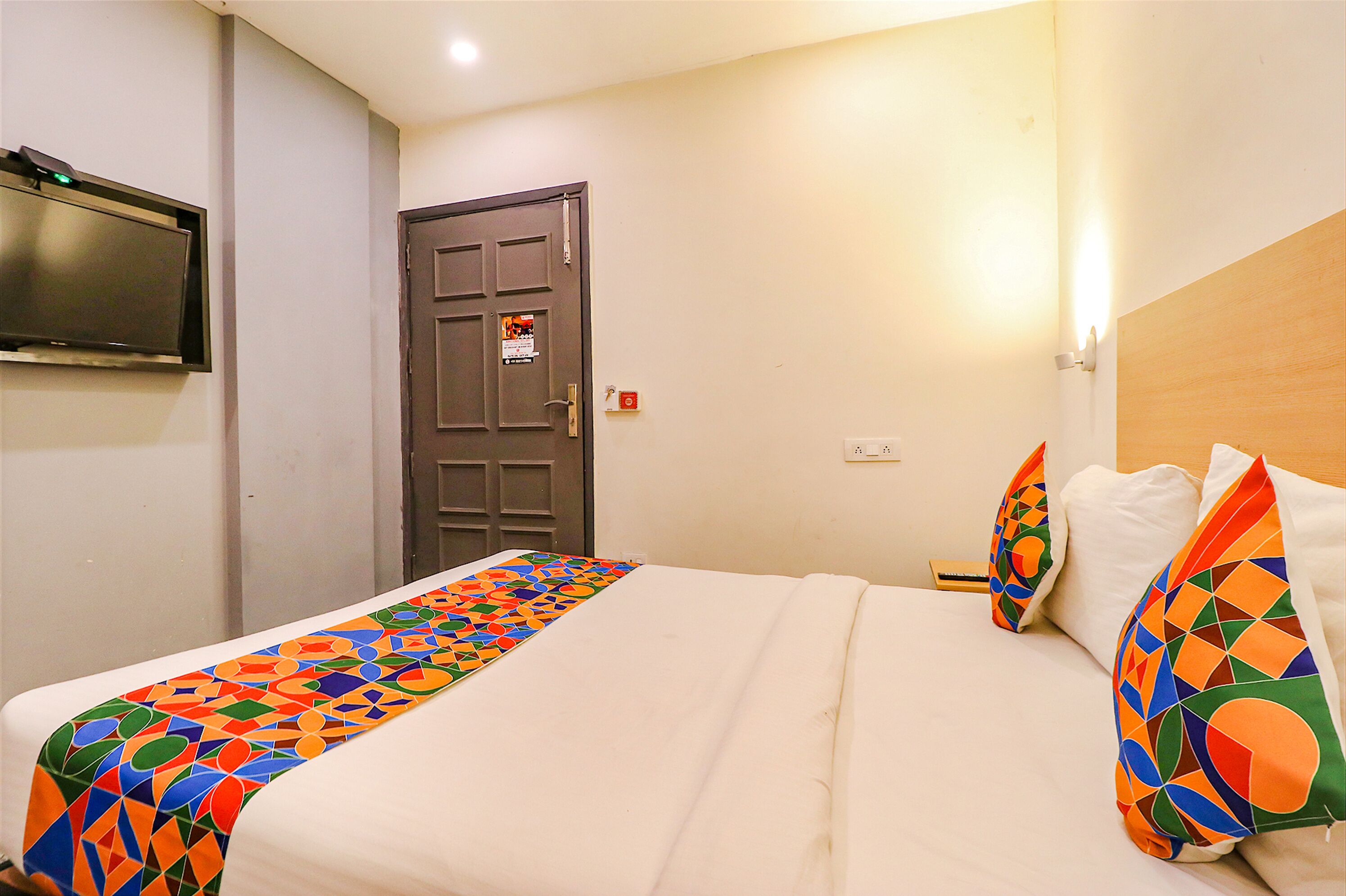 A hotel room with a bed, a TV mounted on the wall, and a door with a sign.
