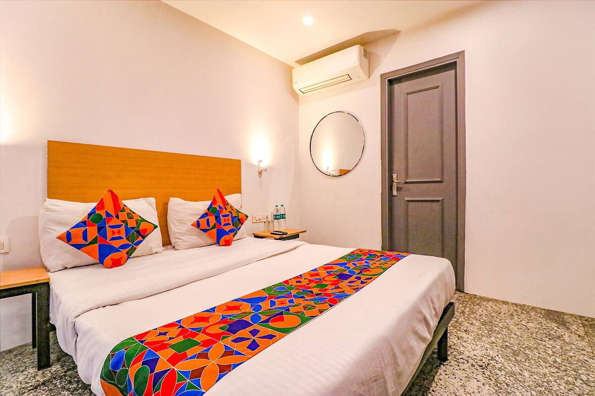 A hotel room with a bed, a nightstand, a mirror, and a door.