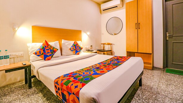 Habitación de hotel con cama, mesita de noche con teléfono y botellas de agua, armario de madera y un espejo redondo en la pared.