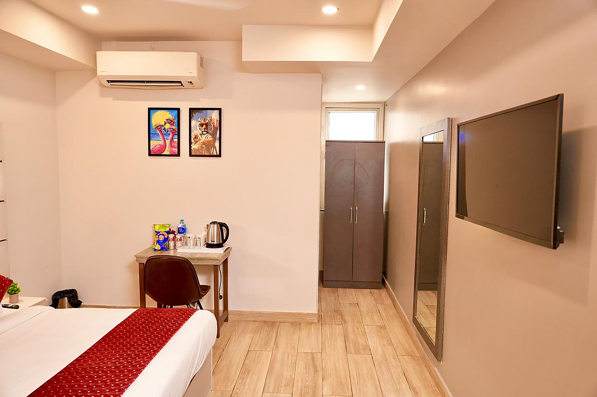 A hotel room with a bed, a desk with a chair, a flat-screen TV, an air conditioner, and a wardrobe.
